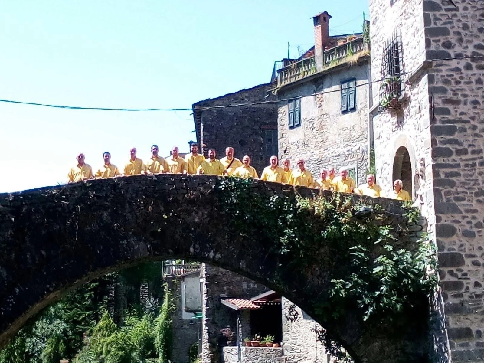 Il Coro La Brughiera con la divisa storica gialla, riunito su un ponte in pietra